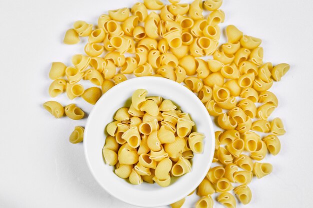 Raw pasta in white bowl and scattered around the white table.