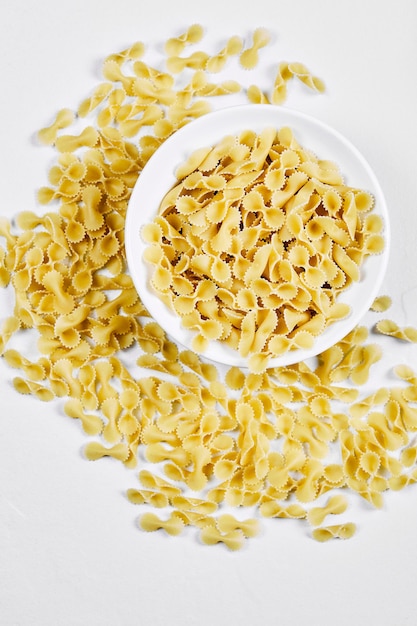 Raw pasta in white bowl and scattered around the white table.