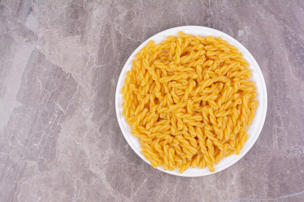 Raw pasta in a white ceramic plate on the marble