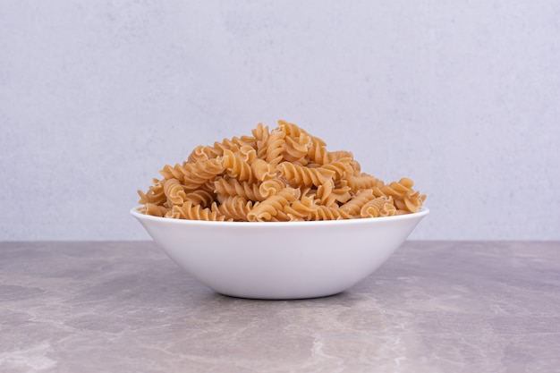 Free photo raw pasta in a white ceramic plate on the marble