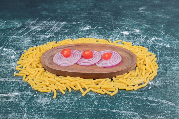 Raw pasta with slices of onion and small tomato on marble space. 