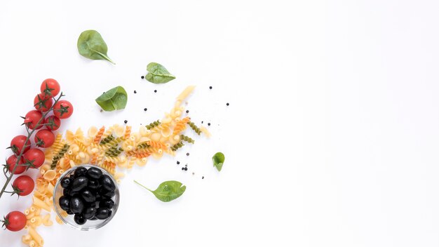 Raw pasta with tomato; black olives; with basil leaf