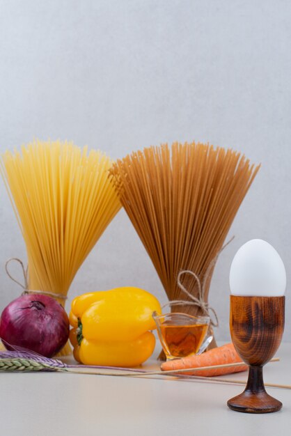 Raw pasta with vegetables on white surface