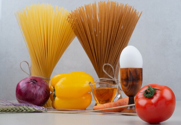 Raw pasta with vegetables on white.