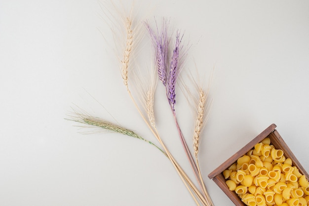 Raw pasta on wooden plate with colorful ears of wheat
