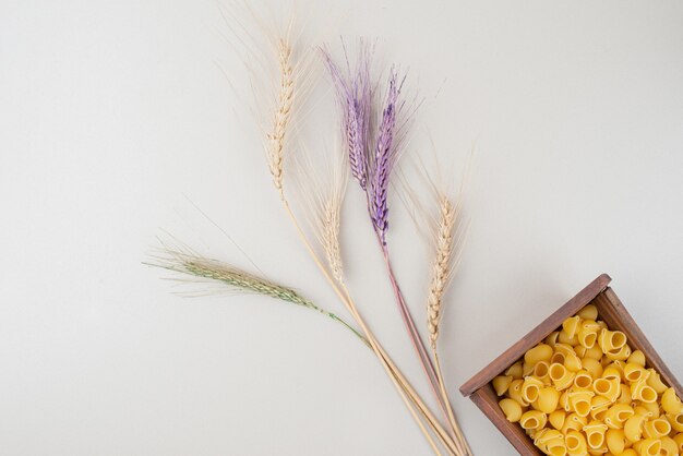 Сырые макароны на деревянной тарелке с разноцветными колосьями пшеницы