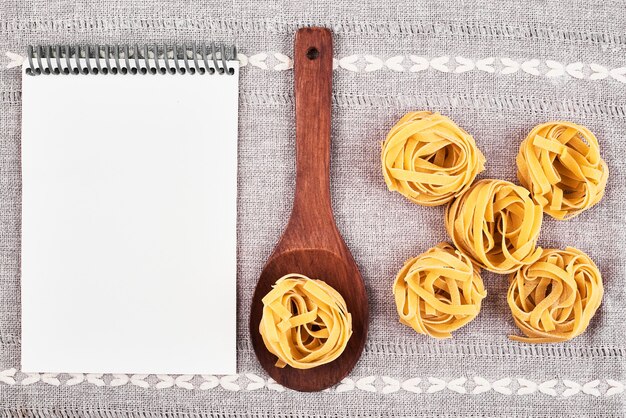 Free photo raw pasta in a wooden spoon with a recipe book.