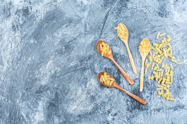 Raw pasta in wooden spoons top view on a grey plaster background