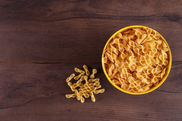 raw pasta in yellow bowl top view on wooden surface