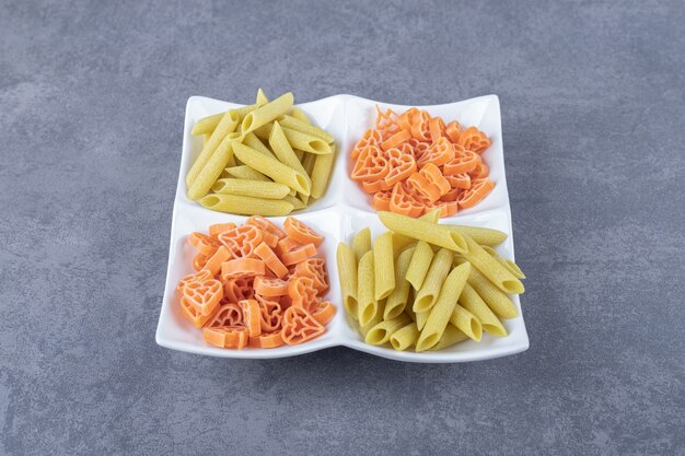 Raw penne and heart-shaped pasta on white plate.