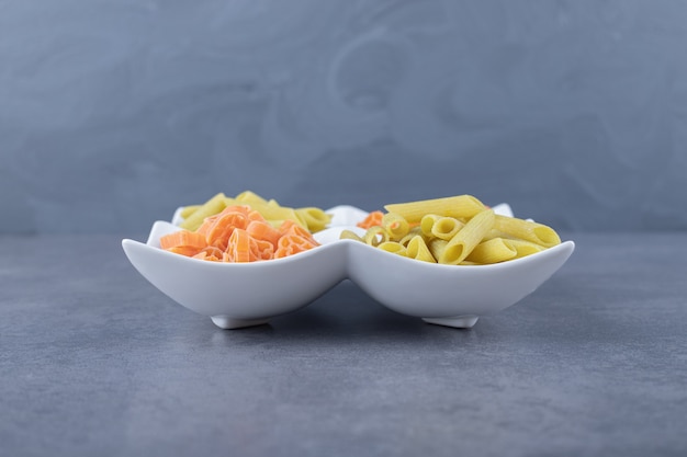 Raw penne and heart-shaped pasta on white plate.