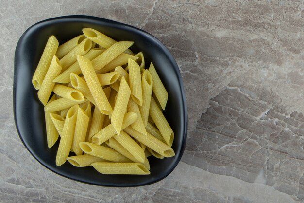 Raw penne pasta in black bowl.