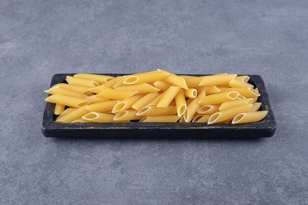 Raw penne pasta on black plate.