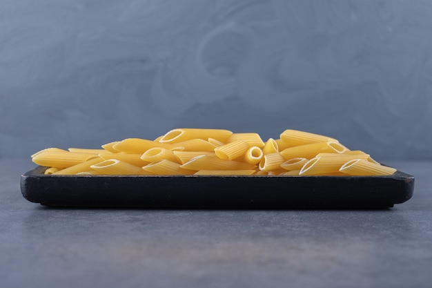 Free photo raw penne pasta on black plate.