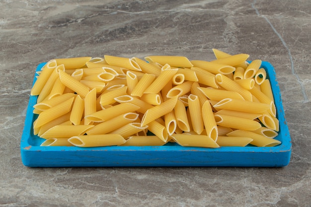 Raw penne pasta on blue plate