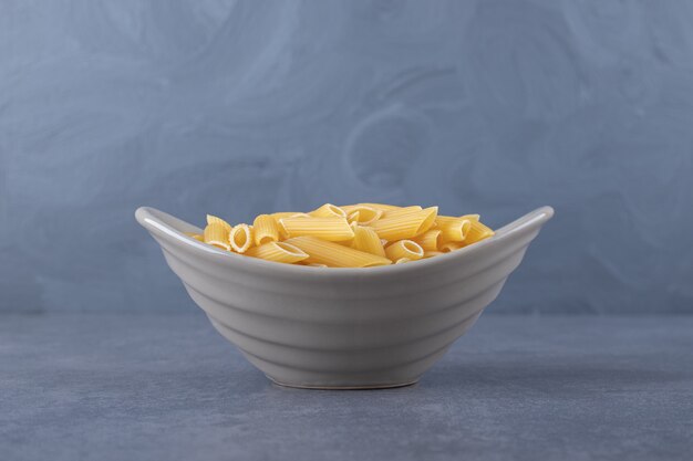 Free photo raw penne pasta in ceramic bowl.