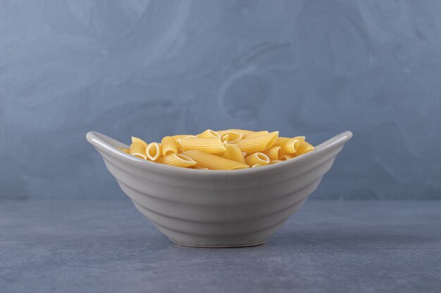 Raw penne pasta in ceramic bowl.