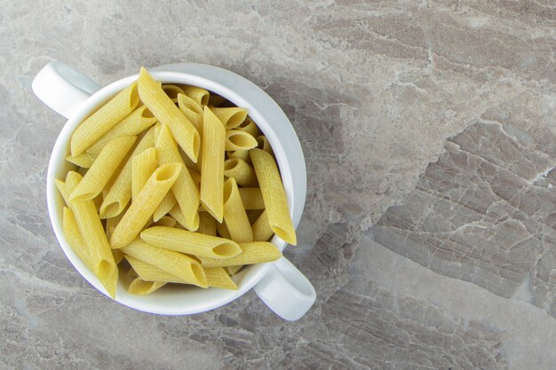 Raw penne pasta in white mug