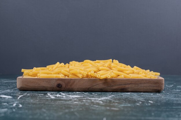 Foto gratuita pasta cruda del penne sul piatto di legno. foto di alta qualità