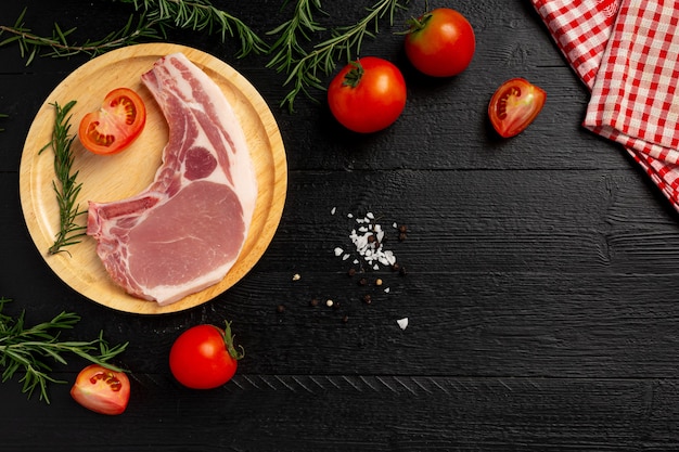 Raw pork chop steak on the dark wooden surface.