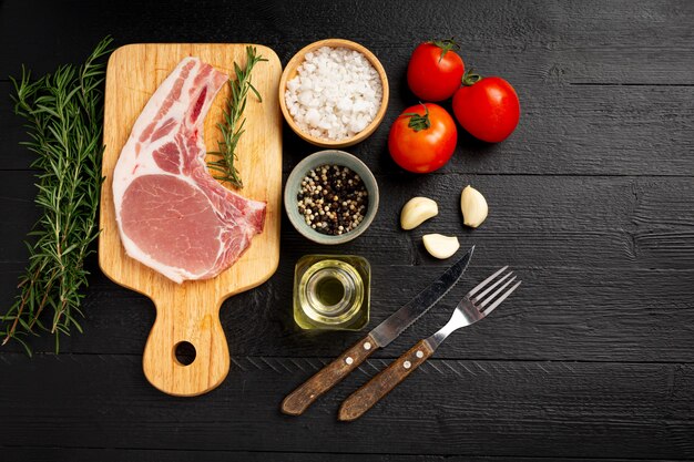 Raw pork chop steak on the dark wooden surface.