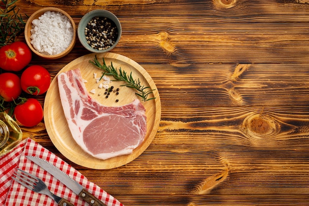 Raw pork chop steak on the dark wooden surface.