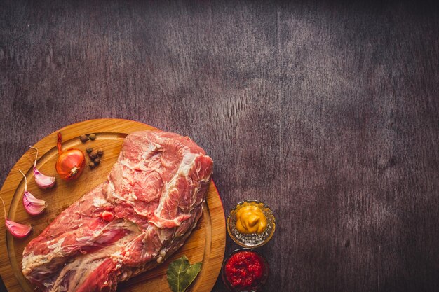 暗い木の表面のまな板に生の豚肉と調理用のスパイス。コピースペースと食品の背景。トーン。静物。フラットレイ。