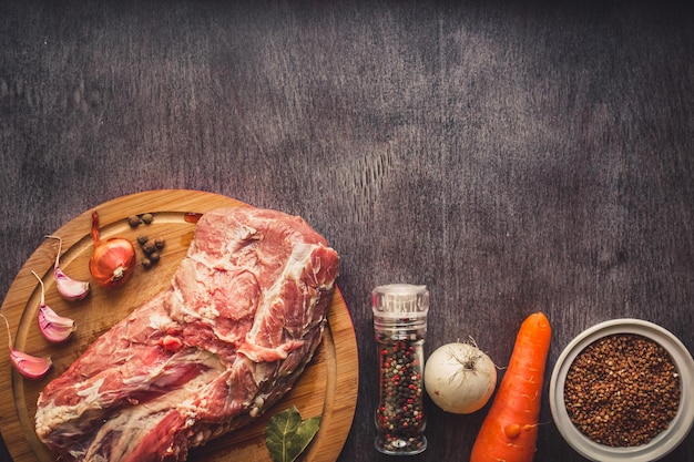 Foto gratuita carne di maiale cruda su una superficie di legno scura e ingredienti per cucinare. sfondo alimentare con spazio di copia. natura morta. disposizione piatta. tonico