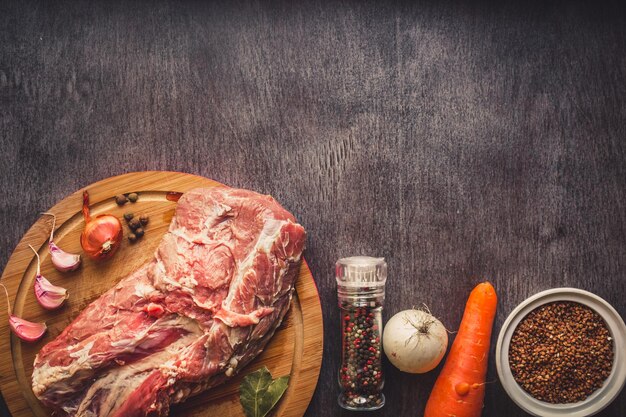 Raw pork meat on a dark wooden surface and ingredients for cooking. Food background with copy space. Still life. Flat lay. Toned