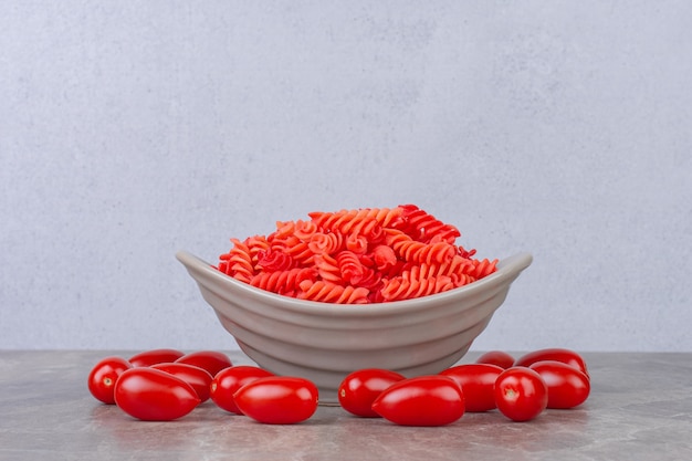 Raw red fusilli pasta in a bowl next to tomatoes, on the marble surface