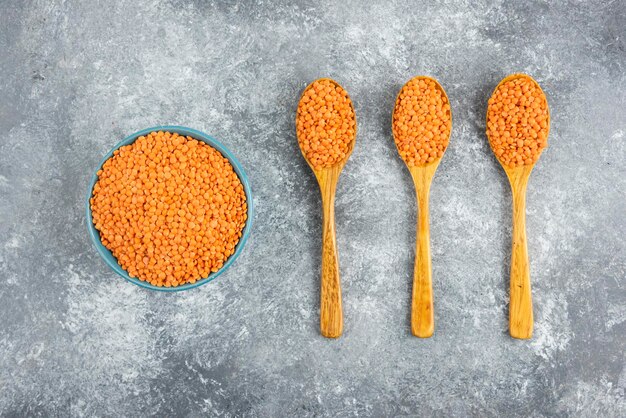 Raw red lentils in bowl and spoons on marble table.