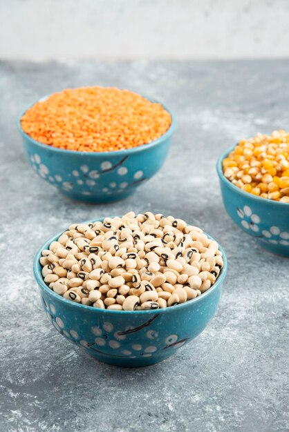 Raw red lentils, corns and white beans in blue bowls.