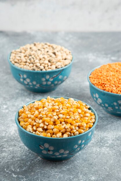 Raw red lentils, corns and white beans in blue bowls.