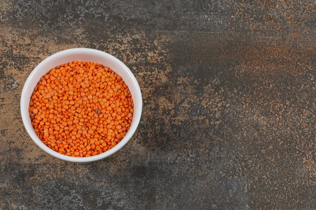 Raw red lentils in white bowl.