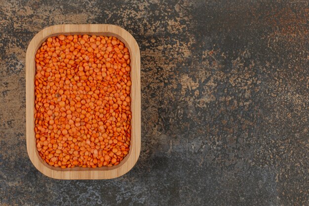 Raw red lentils on wooden plate. 