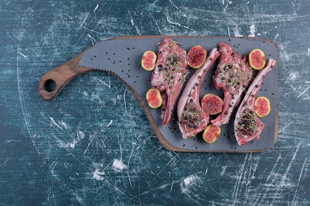 Raw rib chops in wooden board with figs and dried herbs.