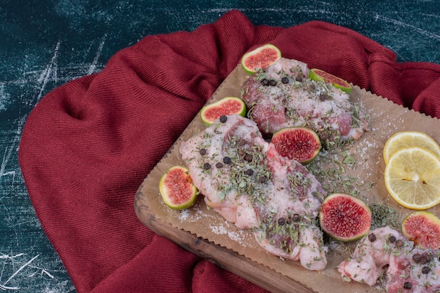 Raw ribs in wooden board with figs, dried herbs and red cloth.