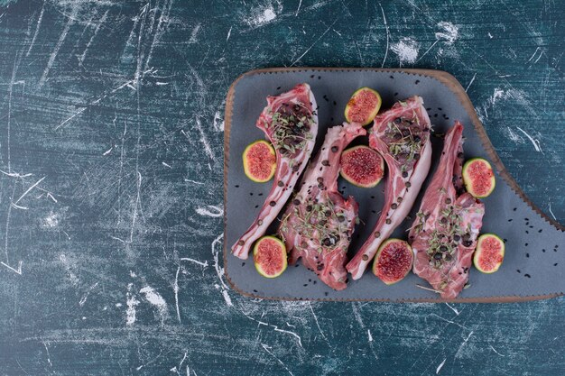 Raw ribs in wooden board with figs and dried herbs.