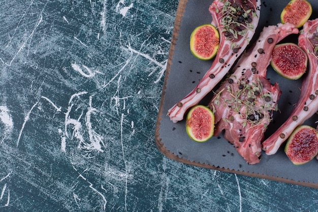 Raw ribs in wooden board with figs and dried herbs.