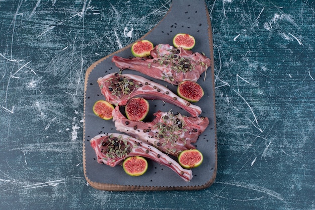 Raw ribs in wooden board with figs and dried herbs.