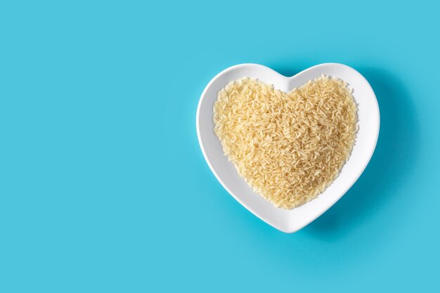 Raw rice on heart shaped plate on blue background