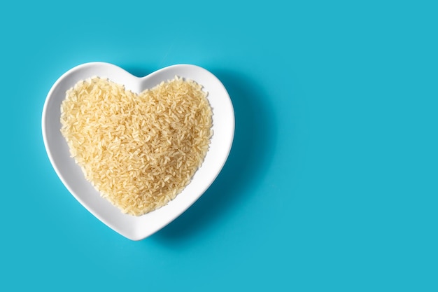 Raw rice on heart shaped plate on blue background