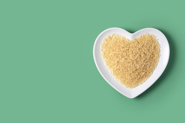 Raw rice on heart shaped plate on green background