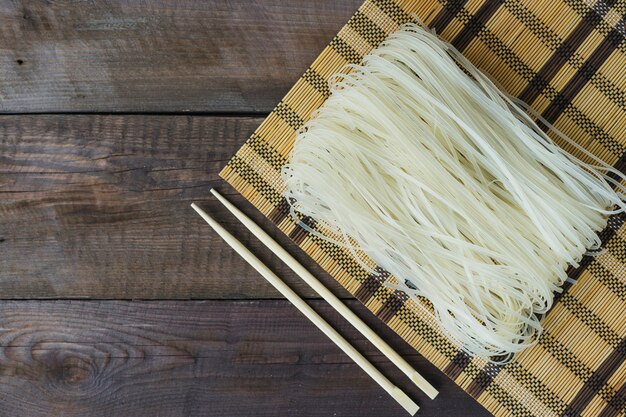 Raw rice noodles in place mat and chopsticks over weathered table