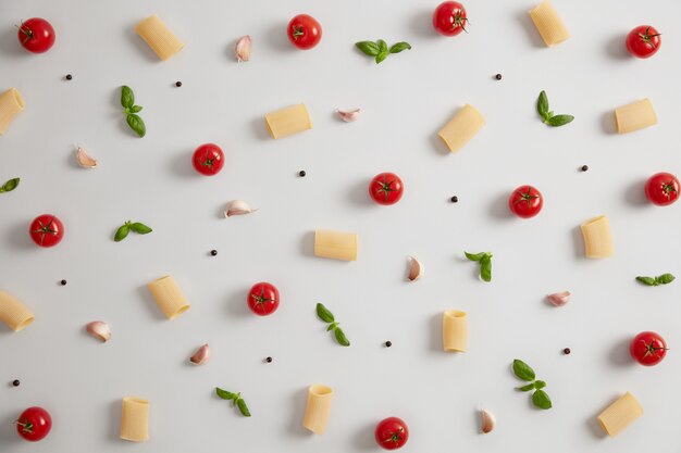 Raw rigatoni pasta made of durum wheat flour, red ripe tomatoes and green basil on white background. Ingredients for Italian cooking. Tradition cuisine. Nourishig pasta dish and food concept