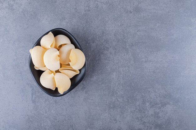 Raw seashell pasta in black bowl.