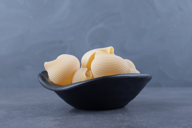 Free photo raw seashell pasta in black bowl.