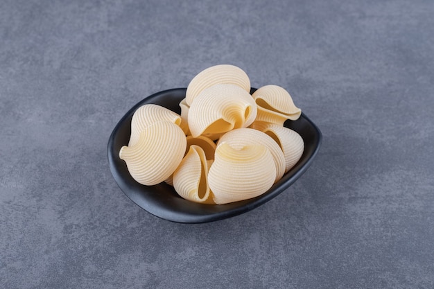 Raw seashell pasta in black bowl.