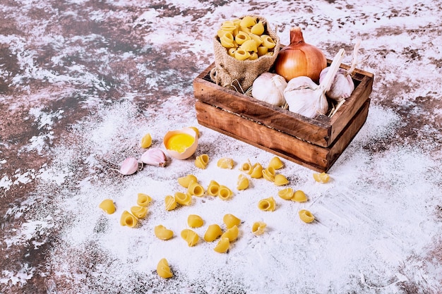 Pasta corta cruda con cipolle e aglio in una tela da imballaggio su una superficie di legno.