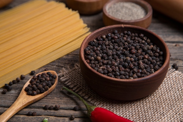 Raw spaghetti and bowl of peppercorns placed on wooden surface. High quality photo